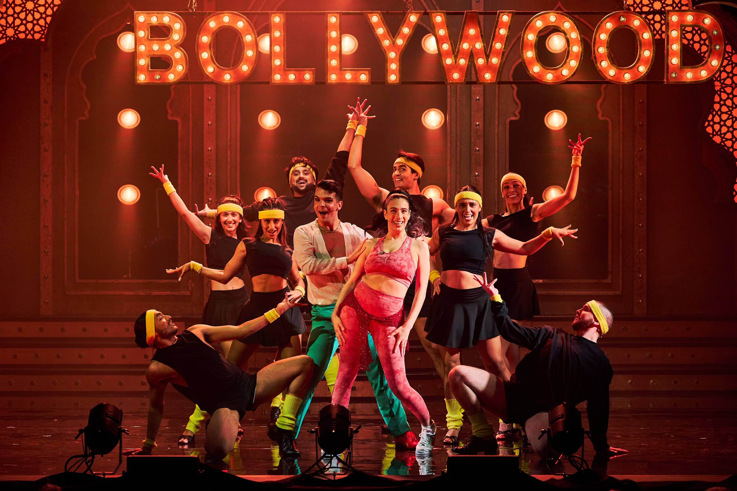 Performers in colorful costumes dance energetically under a bright 