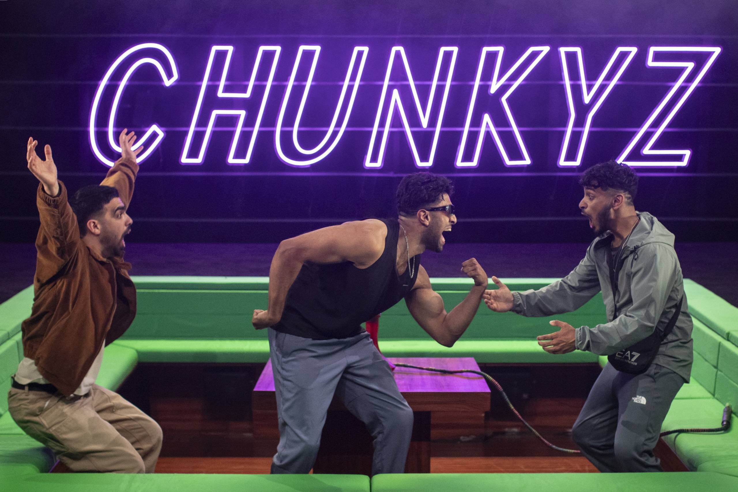 Three excited men celebrating indoors with a neon 