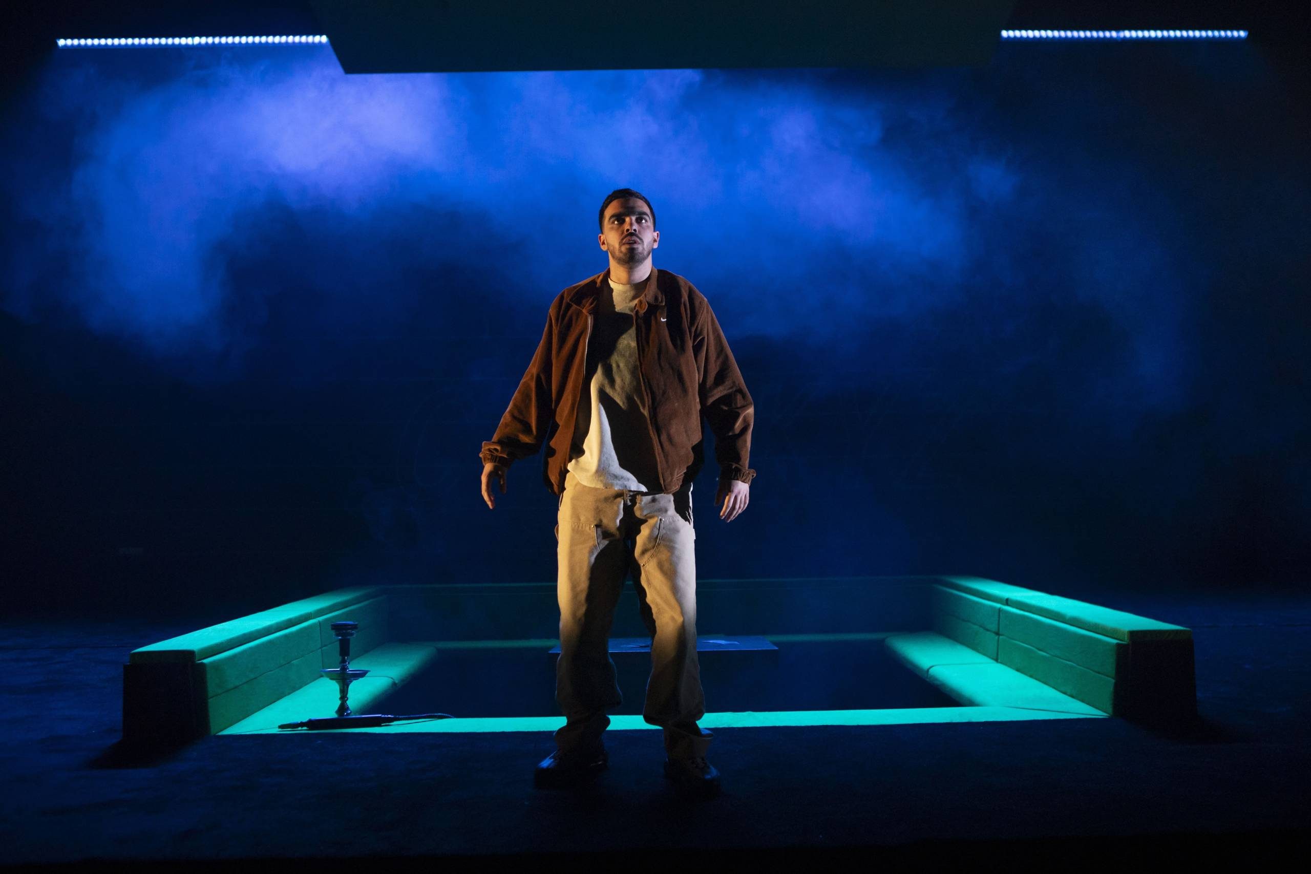 A man stands on a dark stage under blue spotlights and smoke,