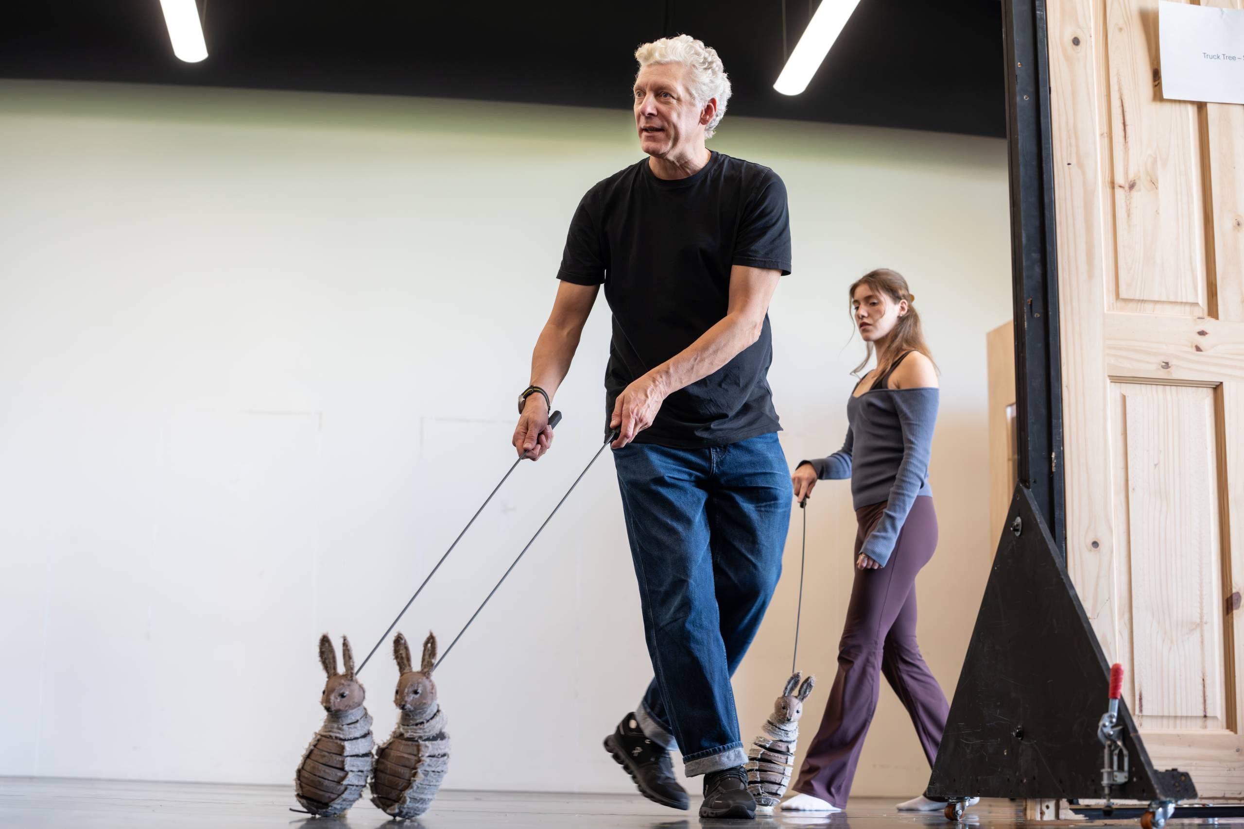 A person is guiding two rabbit-shaped puppets on sticks, with another person walking beside them.