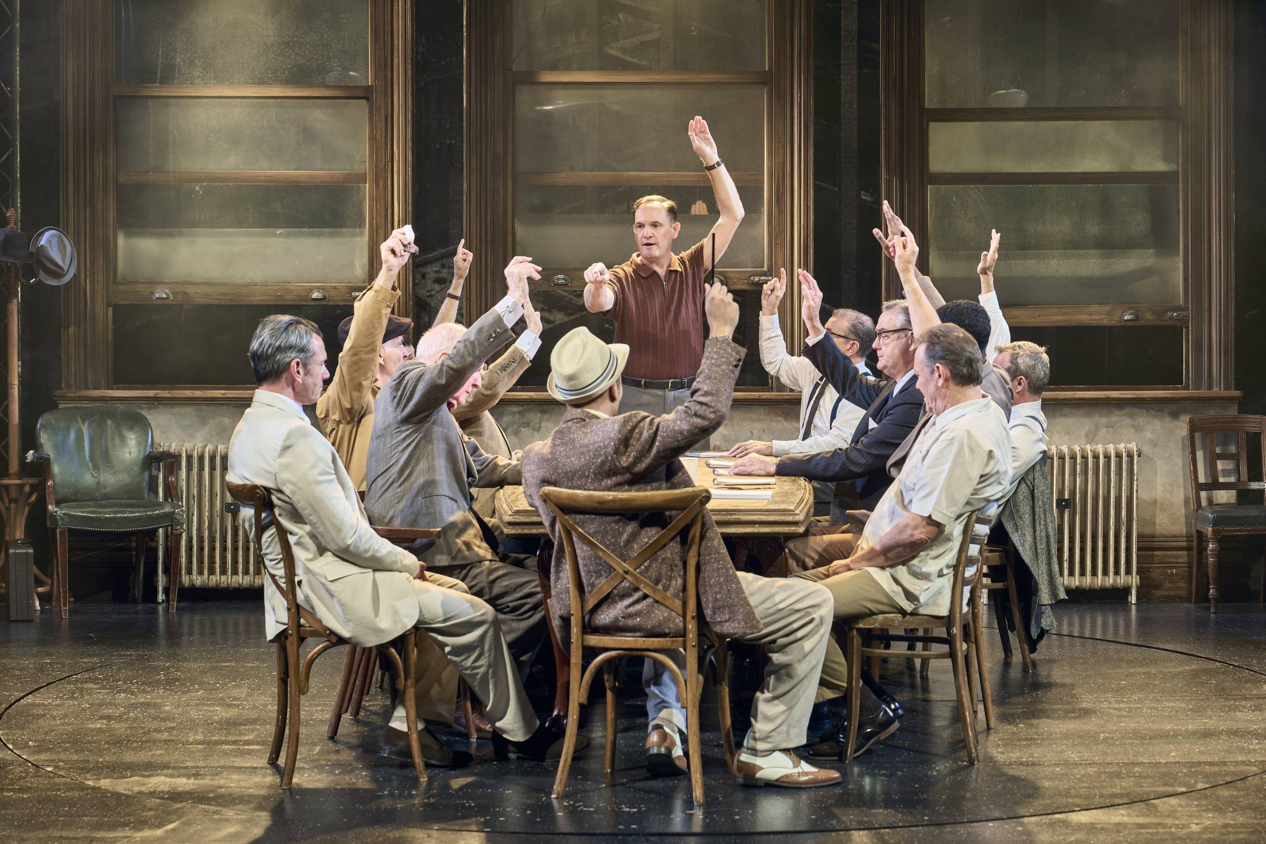 Twelve male Jurors sit around a table, they are taking a vote, all have their hands raised except one.