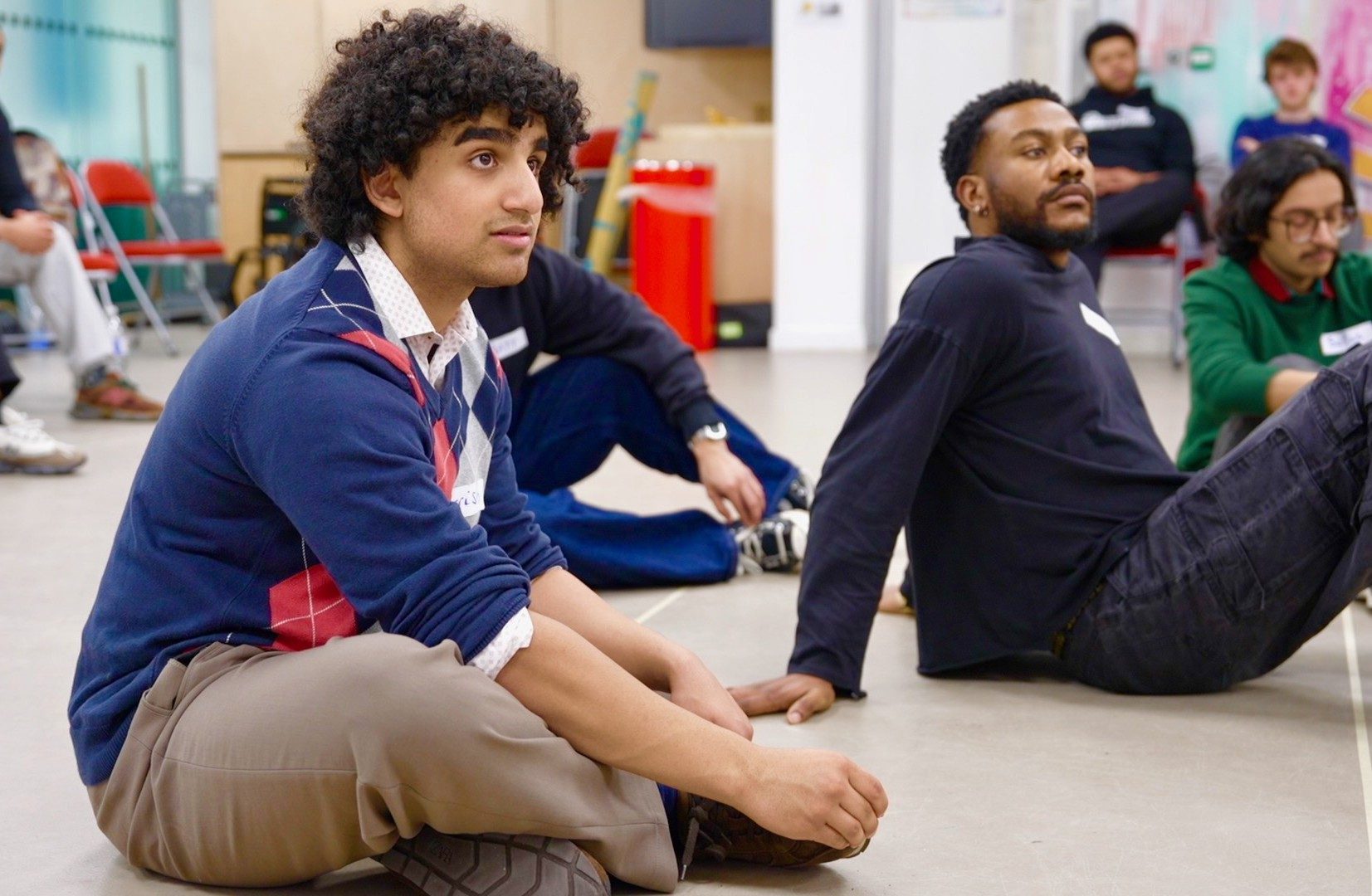 A group of creatives sit on the floor of the rehearsal room.