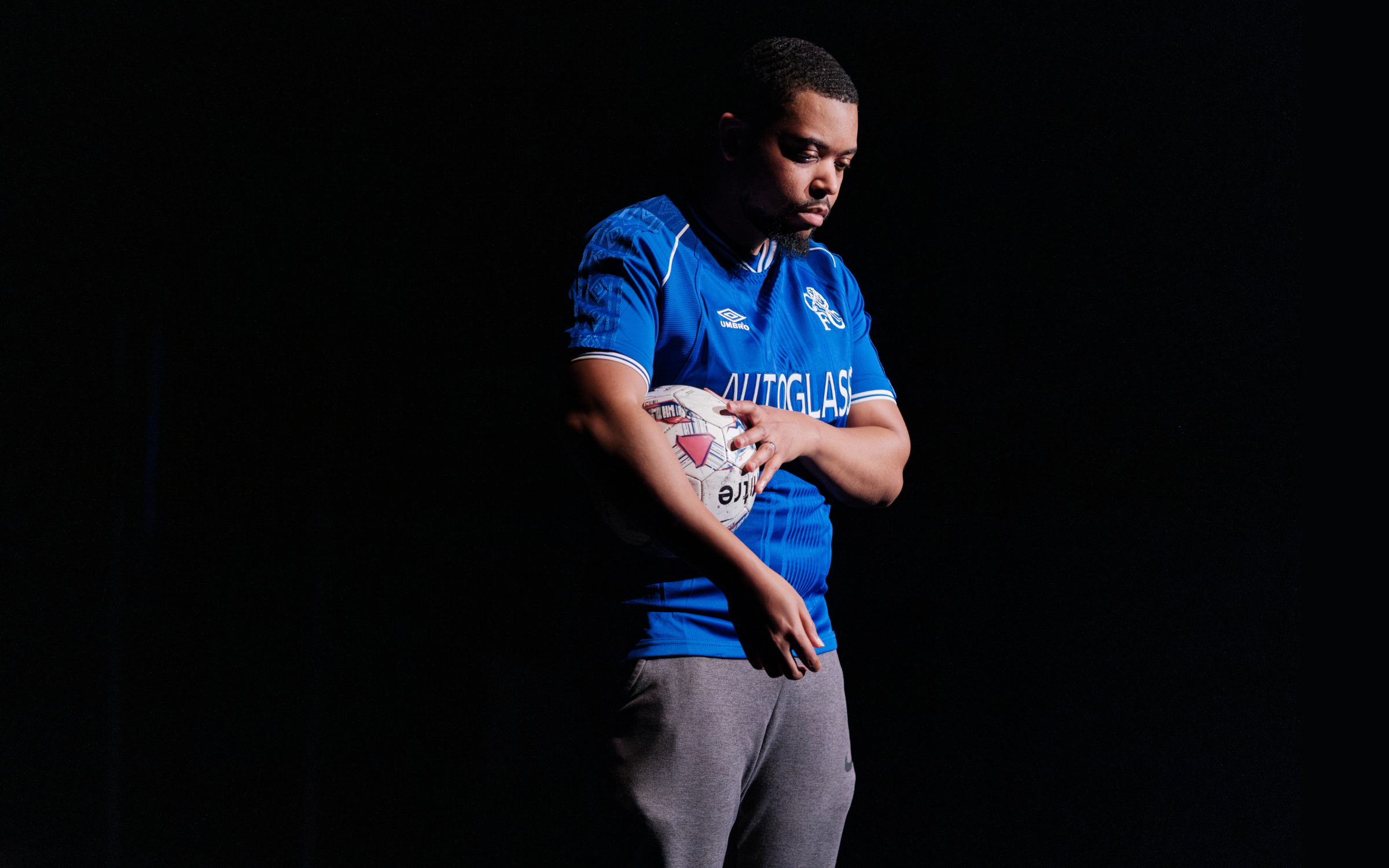 A photo of a young man holding a football and wearing football kit on a black stage.