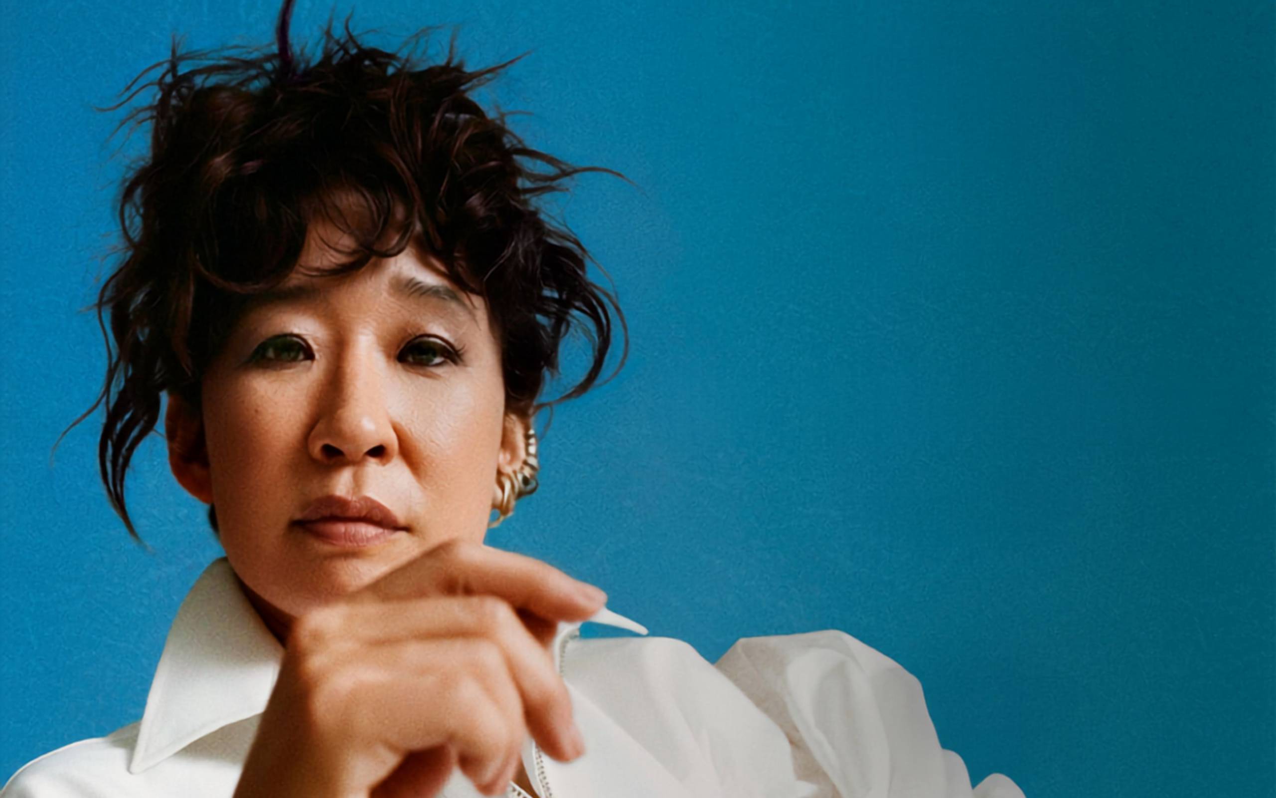 Artwork for The Misanthrope. Close-up portrait of actor Sandra Oh looking directly at the camera with a serious expression, set against a solid bright blue background.