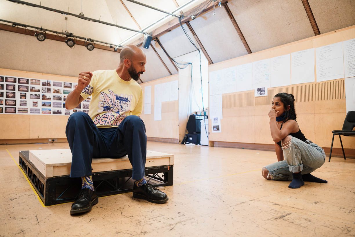 Director Matthew Xia sits on a low platform, engaged in conversation with Linnea Berthelsen sitting on the floor nearby.